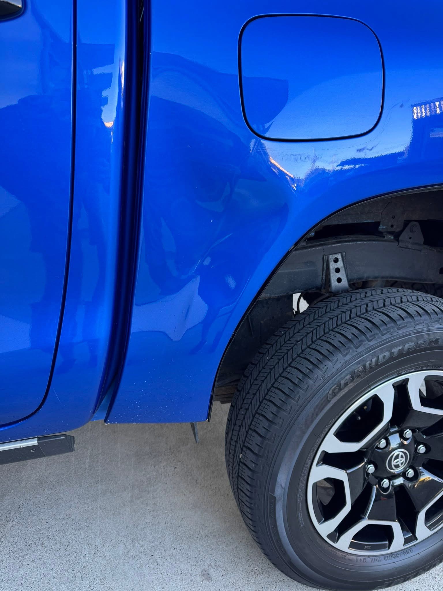 Blue Toyota ute rear quarter panel with a large dent below the fuel door
