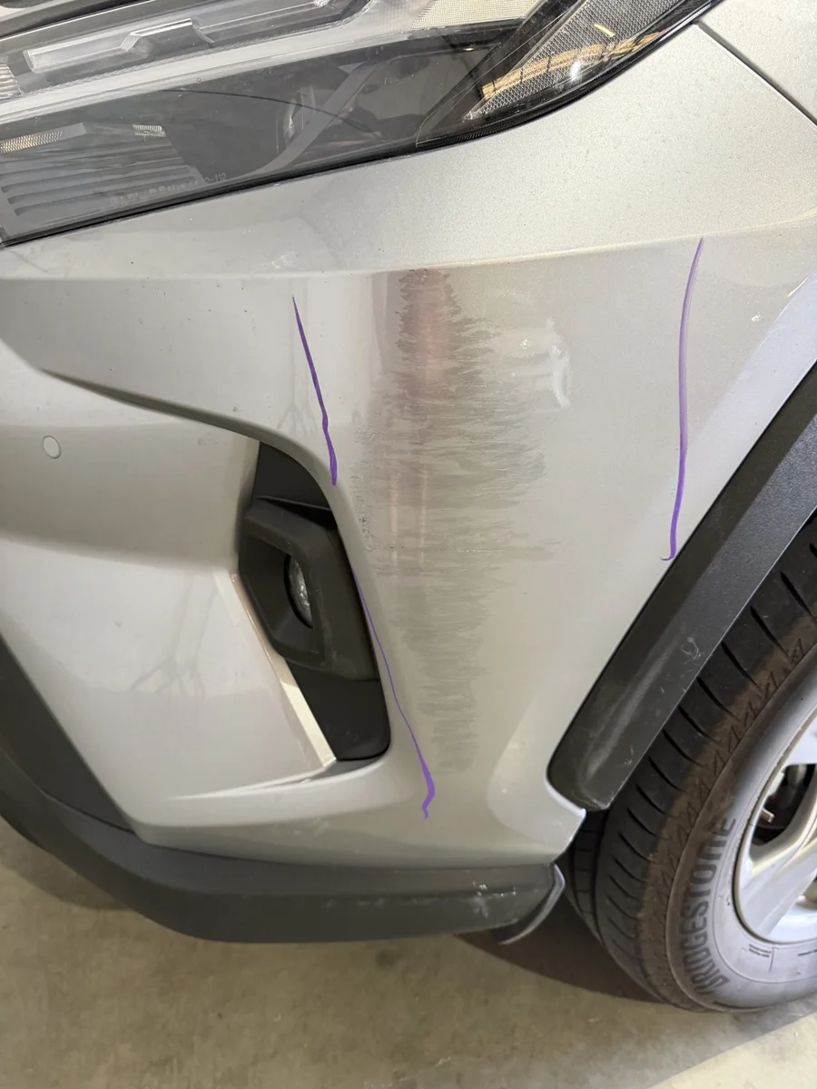 Silver bumper corner before repair with a broad scrape and purple assessment marks