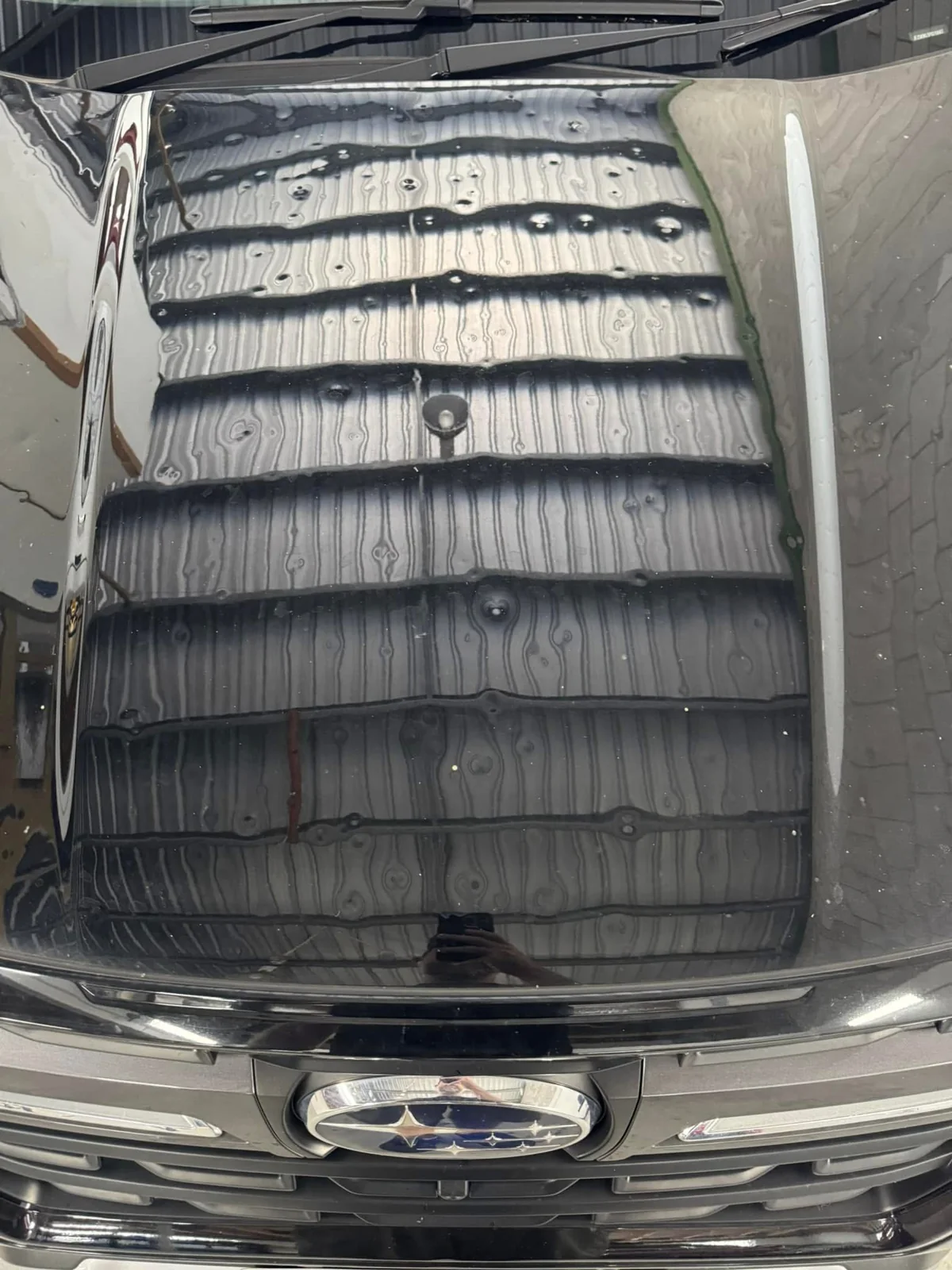 Before repair: dark Subaru bonnet centre view showing hail dents