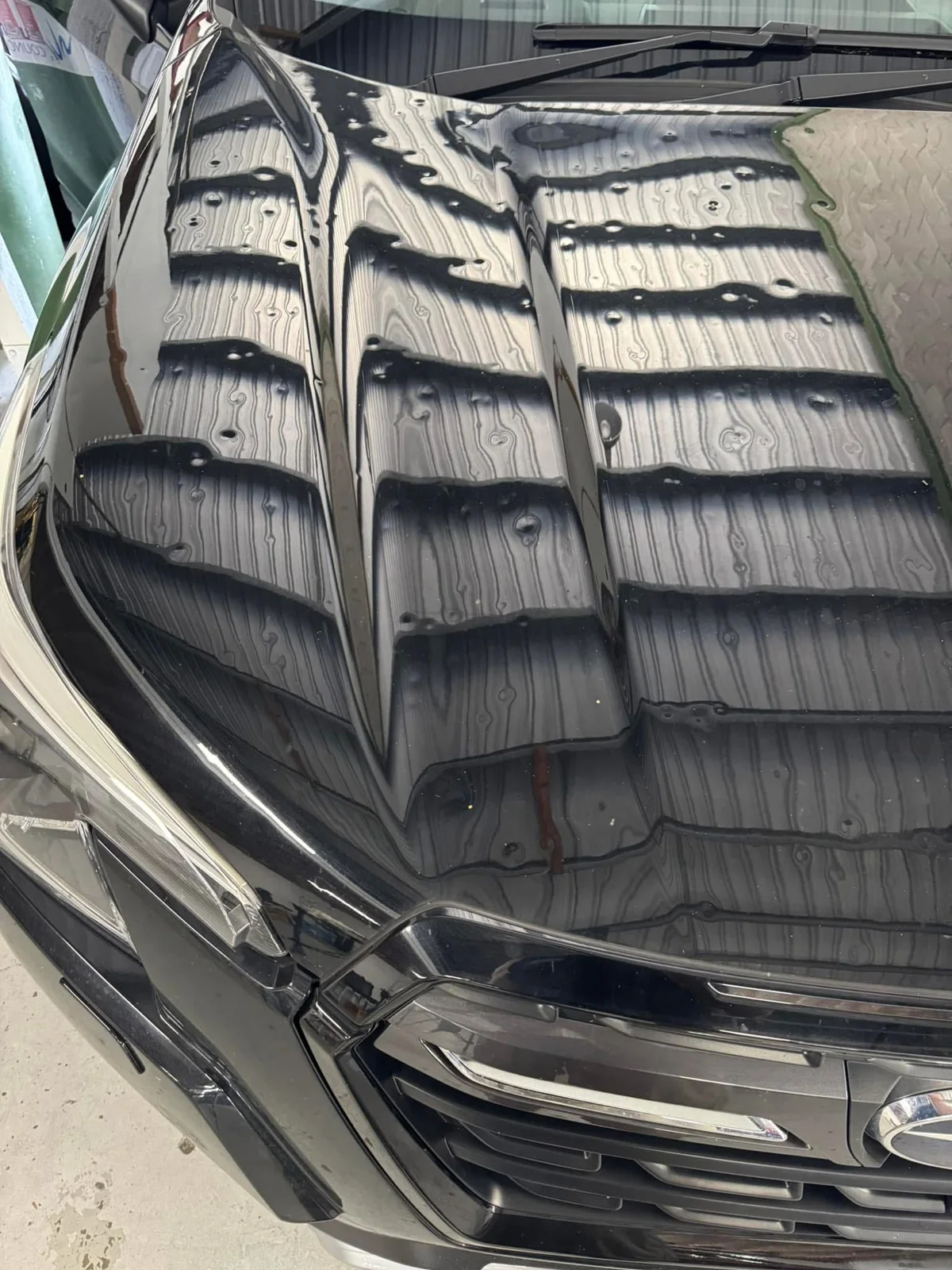 Before repair: dark Subaru bonnet left view showing hail dents