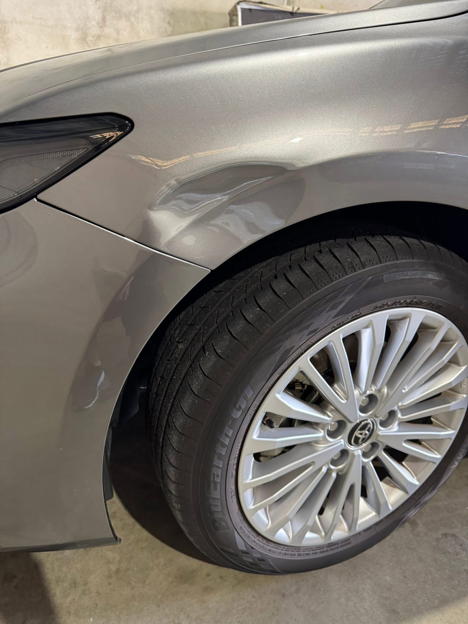 Before repair: a pronounced dent in the grey Toyota front fender above the wheel
