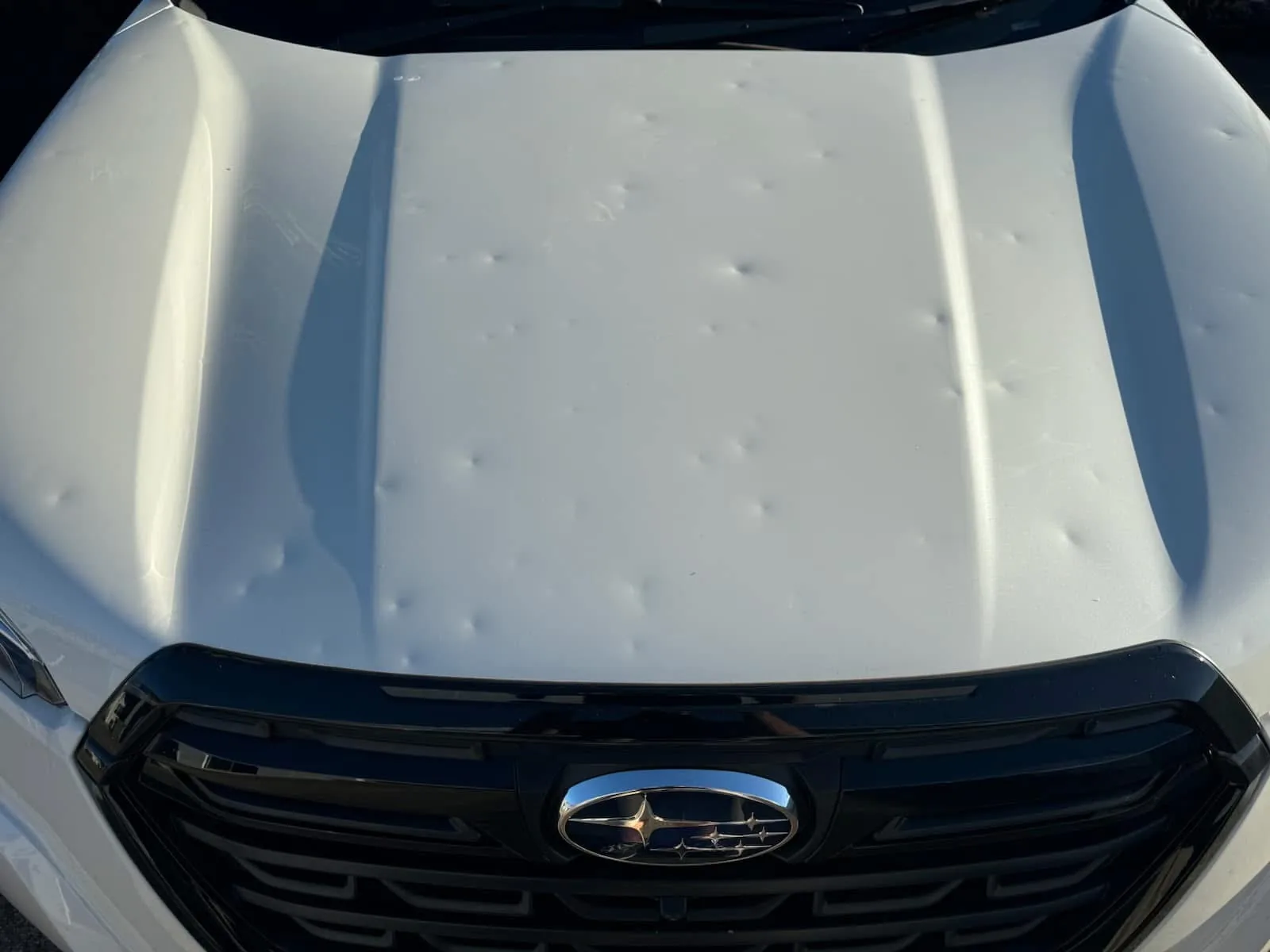 Before repair: white Subaru bonnet with multiple visible hail dents