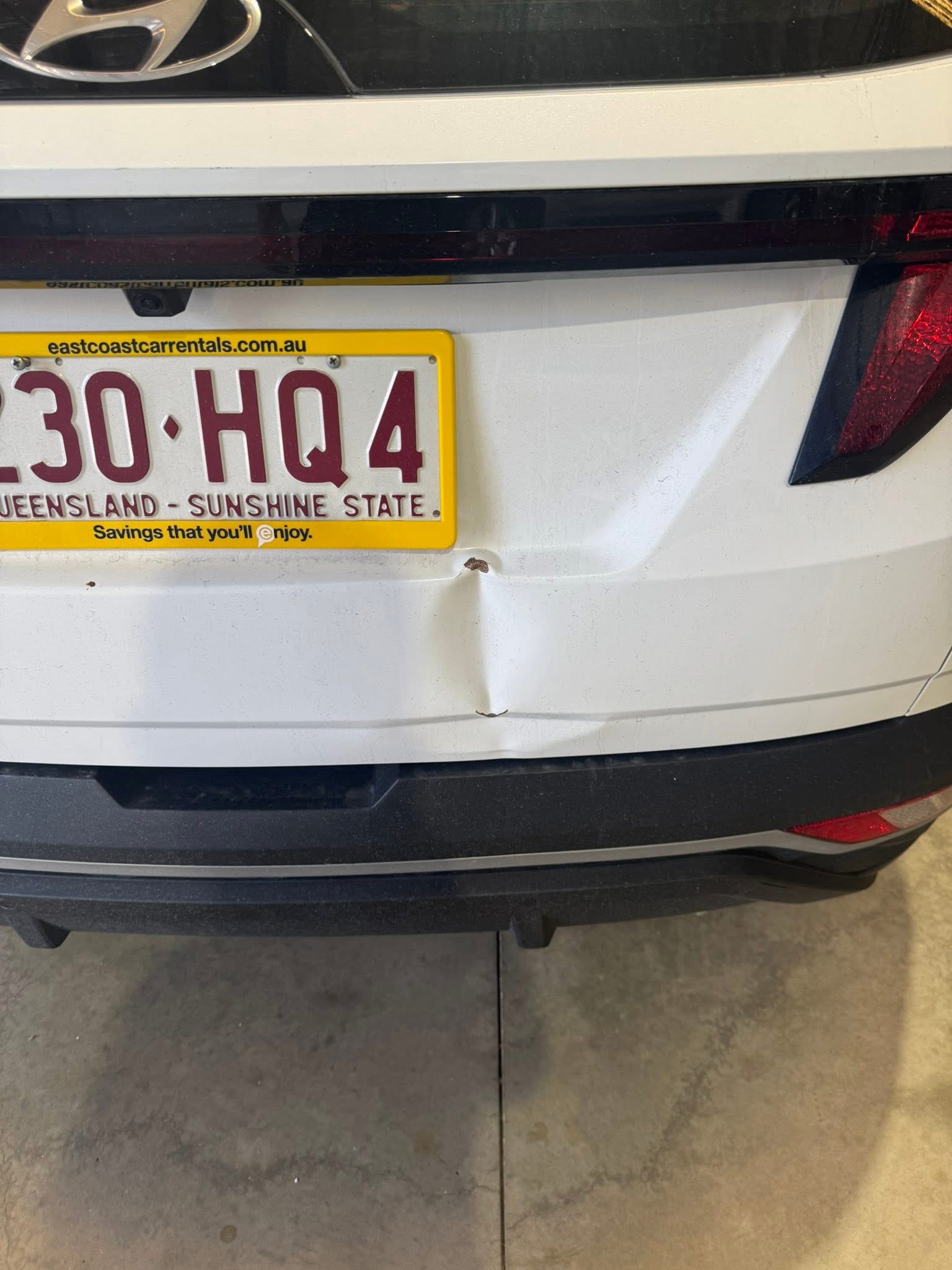 Before repair: white Hyundai rear hatch with a dent beside the registration plate