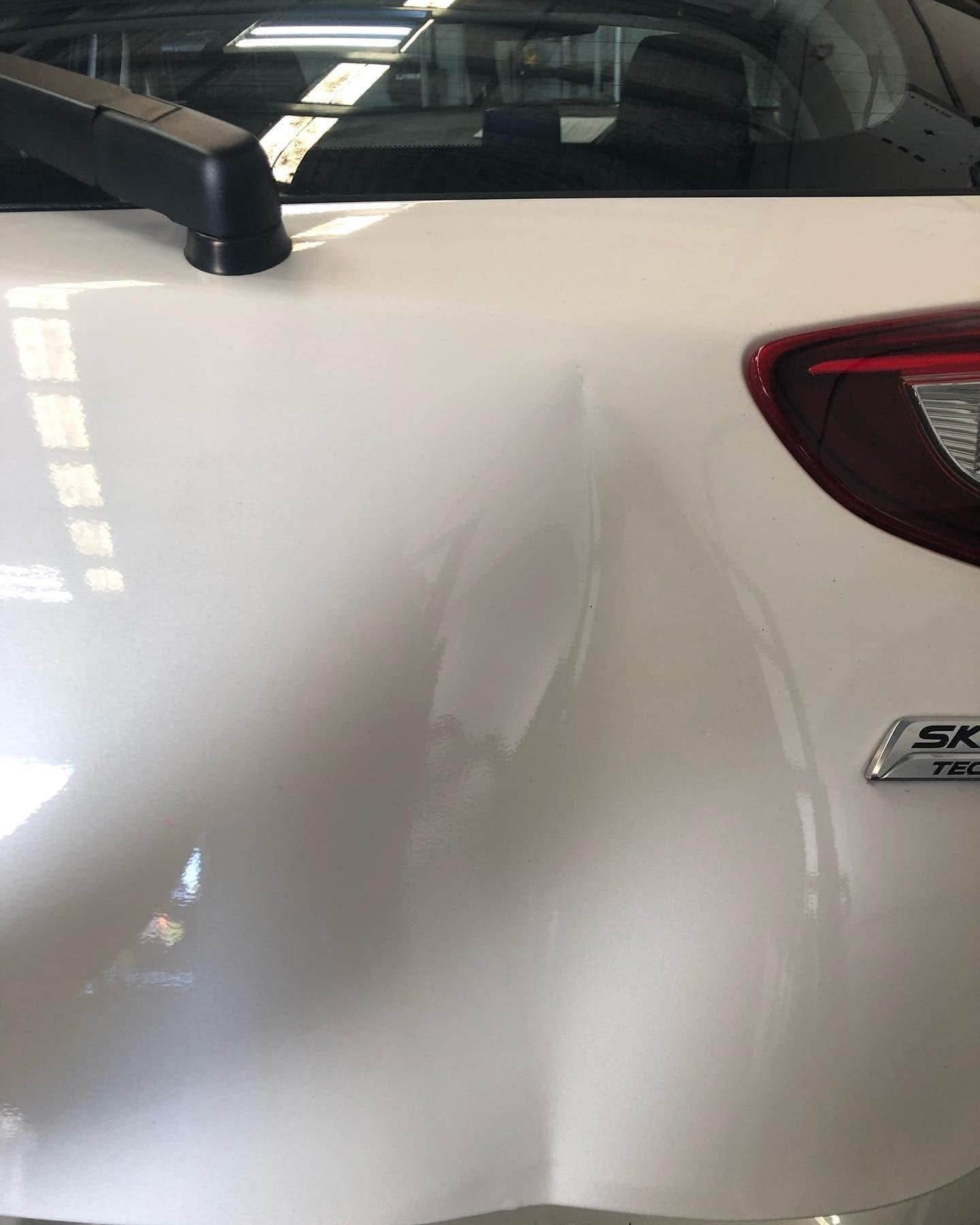 Before repair: wider view of the damaged rear hatch of the white Mazda
